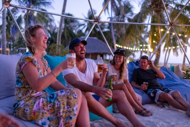 friends laughing around the bonfire on the beach at sunset friends laughing around the bonfire on the beach at sunset
